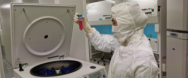 A gowned technician inspecting a sample vial beside an open centrifuge in a NiSCELL cleanroom.