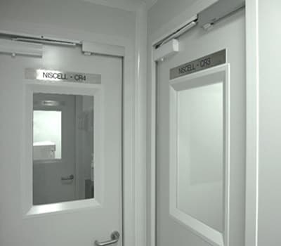 Two cleanroom entry doors with viewing panels, each carrying an engraved sign reading NISCELL CR4 and NISCELL CR3.