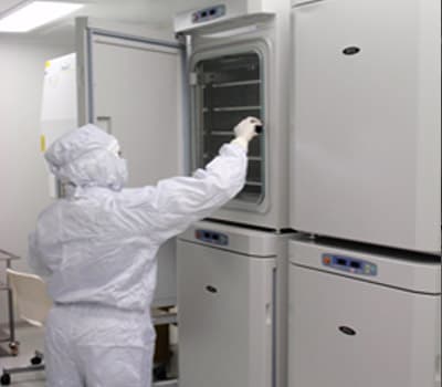A gowned operator reaching into an open upper cabinet among stacked white units with digital control panels.