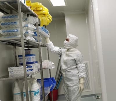 A gowned technician retrieving supplies from a shelved storage rack inside a cleanroom.
